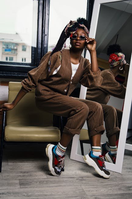 Trendy black woman wearing sunglasses and sneakers posing in a studio.