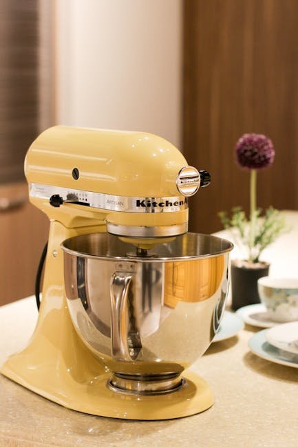 Vibrant yellow stand mixer on a kitchen countertop beside tableware and decor.