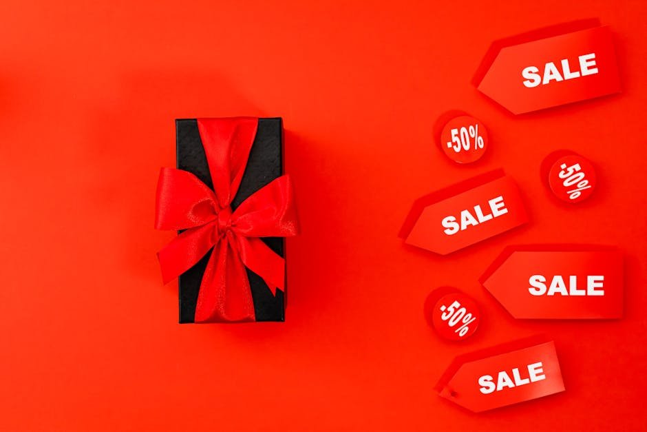 A black gift box with a red ribbon surrounded by sale tags on a vivid red background, showcasing a discount theme.