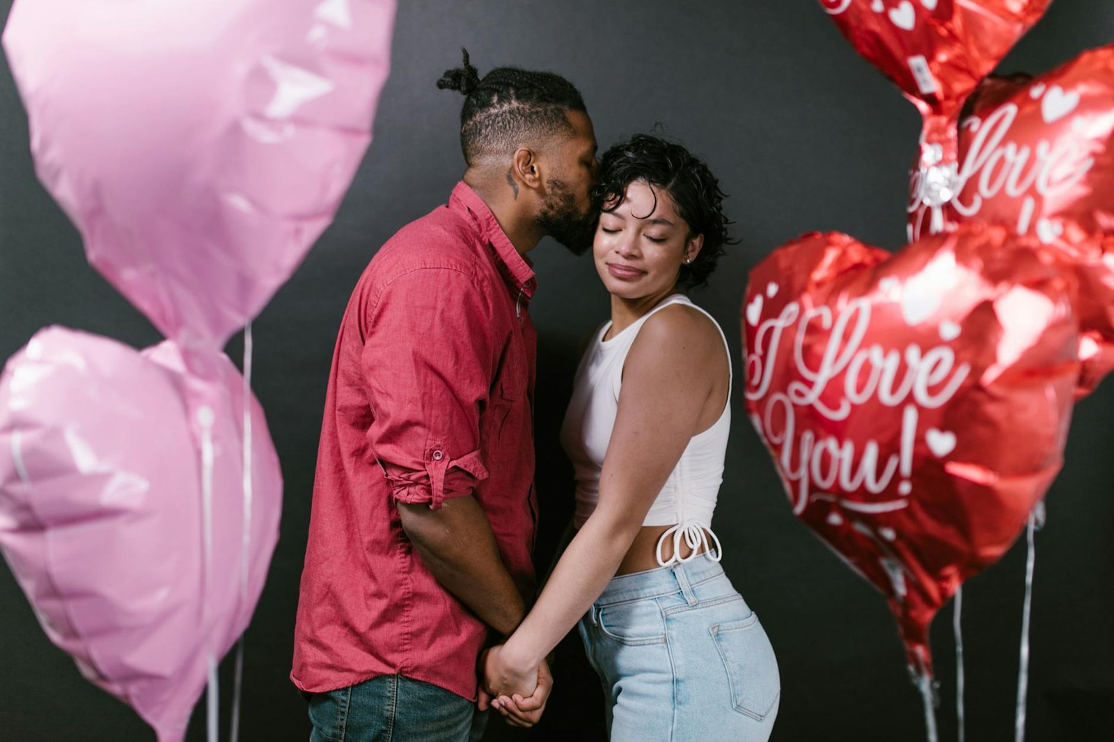 Romantic couple holding hands surrounded by heart-shaped balloons, celebrating love.