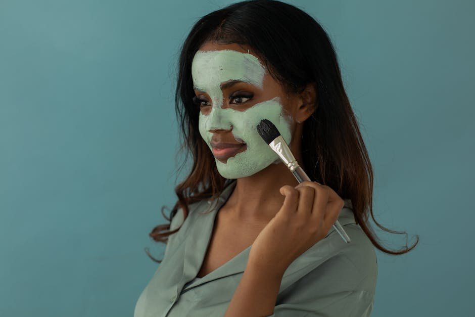 Smiling woman applies facial mask with a brush against a blue background.